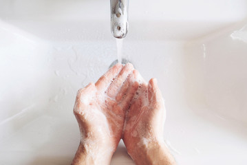 Man cleaning his hands using liquid disinfectant soap and water in bathroom.