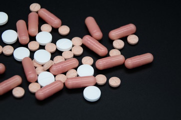white and pink tablets and pink and yellow capsules on a black background. Coronavirus Covid-19. Copyspace.