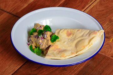 Meat with gravy and fresh greenery served with a piece of lavahs bread on white plate over dark rustic background.