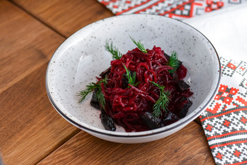 Traditional Ukrainian beetroot salad served in white bowl over rustic wooden table with traditional tablecloth.