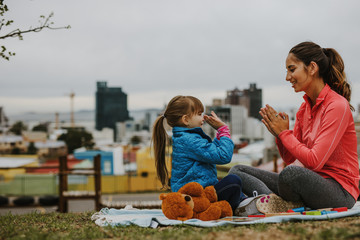 Girl playing patty-cake game with her nanny outdoors - obrazy, fototapety, plakaty