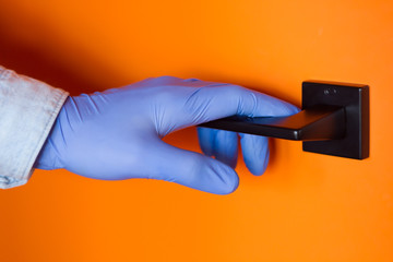 Closeup male hand in medical gloves is opening door, holding knob. Virus SARS-CoV-2 , 2019-nCoV are in air around, on surfaces. Prevention and hygiene rules during pandemic of coronavirus covid-19.