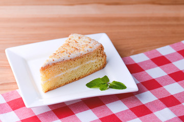 Slice of victoria sponge cake with cream filling, served with a mint leaf on a white plate on light wooden table