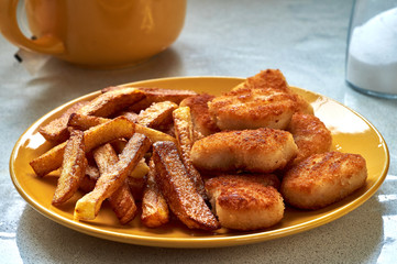 Tasty homemade potato french fries with chiken nuggets on yellow dish