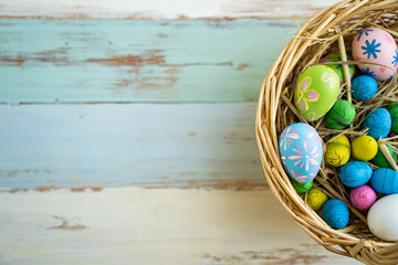 flat lay of colorful vibrant easter eggs with stripe and flower pattern painted on, laying on bird nest basket with straw hays, blue wooden table background representing celebrating easter holidays