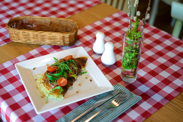 Omelette with vegetables served on a square white plate over red plaid tablecloth background with cutlery.