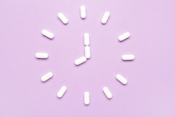 Clock made of sleeping pills on color background