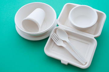 Natural eco-friendly disposable utensils (fork, spoon, dish plate, bowl, cup and fast food box container) made of fiber of bagasse and bamboo on green background with copy space. Save the earth.