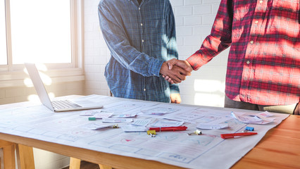 close up male asian ui/ux designers hand shaking each other working and designing a user interface for website and application as partner planning and brainstorming sketch designs with computer laptop
