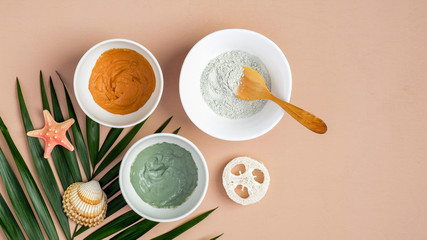 Homemade clay mask recipe concept. Top view cosmetic facial masks in bowls and tropical leaf on peach background. Face skin care, spa products, beauty treatment