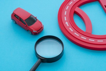Red car, road and magnifying glass on blue background. Auto insurance business concept. Check car...