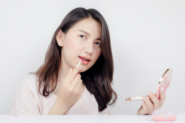 A beautiful Asian model is using lipstick.