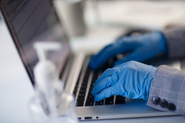 Close up of hands in protective gloves working from office or home using laptop on desk. Preventing corona virus covid-19 spread during epidemic outbreak