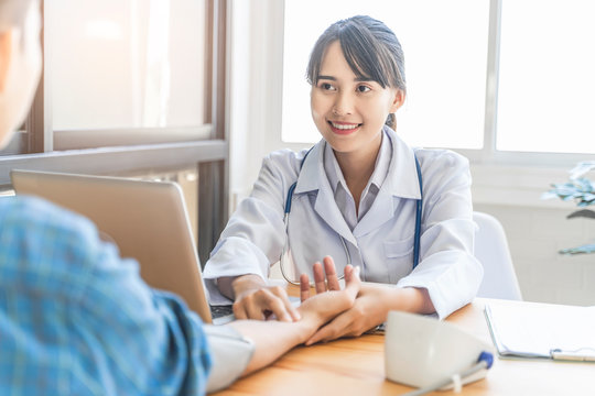 asian female doctor working in hospital office talking to patient, checking blood pressure of patient with two fingers on wrist, documentations of symptoms, health insurance and medical care contract