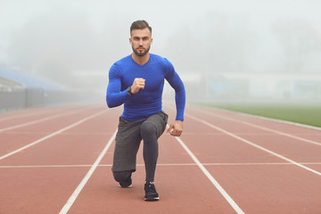 Fototapeta premium The guy the athlete does squats in the stadium in the fog
