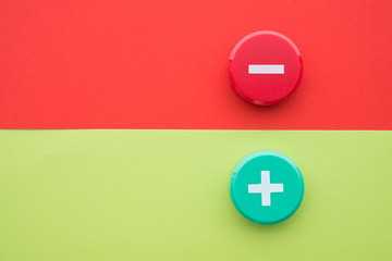 Flat lay of green plus and red minus symbol plastic botton on green and red background with copy space. Concept of difference, opposites plus vs minus or pros vs cons.