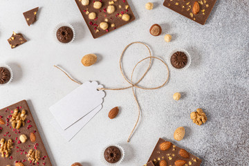Homemade milk chocolate bars and pralines with dried berries and nuts on light background. Top...