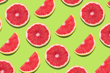 Flat lay fruit pattern of fresh grapefruit slices on green background.