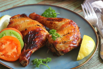 Food background. Grilled chicken leg quarters with crispy golden brown skin, lemon and vegetables for celebration and holiday