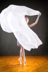 Young woman ballerina dancing with white fabric in the studio.
