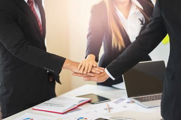 asian businessmen and businesswomen putting hands together piling on top of one another representing teamwork, community, help and support within the business or company within an office environment