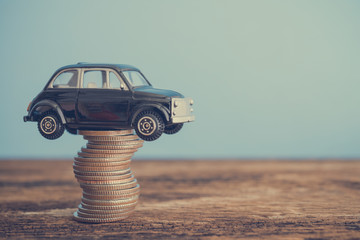 Miniature black second hand car model on coins stack on wooden table. Business, finance or budget...