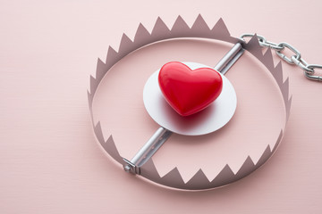 Red heart in a trap on pink background. Online internet romance scam concept. Love is bait or...