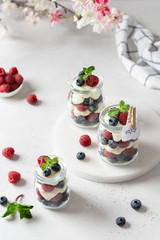 Healthy breakfast. Glass jars with tasty parfaits made of raspberries, blueberries and yogurt on white table. Confectionery menu