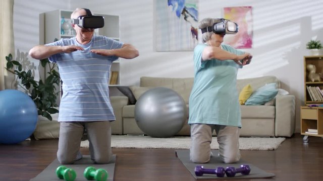 Sportive senior man and woman in VR glasses doing torso rotation exercise on mats in the living room while training together at home