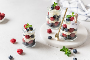 Healthy blueberry and raspberry parfait in mason jars on a white concrete background. Summer, spring dessert. Side view. Recipe, menu