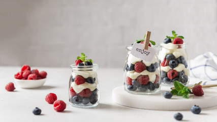 Confectionery banner. Sweet summer berry dessert. Trifle with cream cheese, raspberry and blueberry served in jars on white background. Copy space