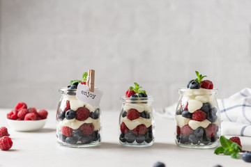 Obraz na płótnie Canvas Fresh berry trifle. Raspberry and blueberry parfait with cheese cream and mint served in glass jars on white background. Summer dessert. Confectionery menu. Copy space