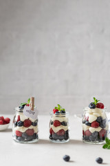 Sweet homemade dessert parfait or trifle with raspberries and blueberries served in glass jars. Summer dessert, confectionery menu. Copy space