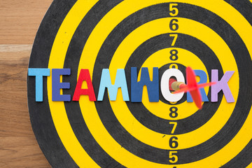 Color alphabets TEAMWORK acronym on dartboard background with red arrow hit center of target. Business strategy and management concept. Teamwork is key success of business target.