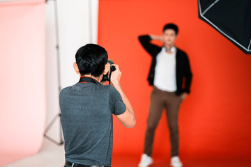 back view of male asian professional photographer taking picture of male model in red isolated...