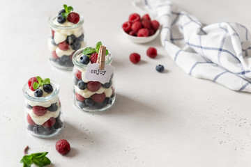 Sweet homemade dessert parfait or trifle with raspberries and blueberries served in glass jars. Summer dessert, confectionery menu. Copy space