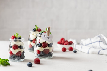 Fototapeta na wymiar Fresh berry trifle. Raspberry and blueberry parfait with cheese cream and mint served in glass jars on white background. Summer dessert. Confectionery menu. Copy space