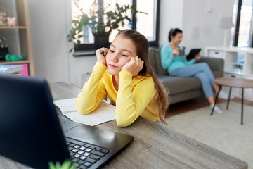 children, education and distant learning concept - bored student girl with laptop computer and notebook and mother with tablet pc at home