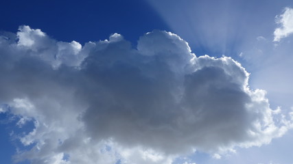 Naklejka na ściany i meble Sunbeams shining through clouds against blue sky with beautiful clouds