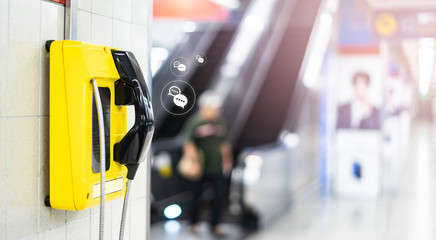an emergency yellow land line phone cell on wall in public area of subway underground transport train station, concept of emergency calling situation on needing to contact people in urgent action