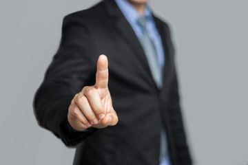 closeup concept of a male asian businessman standing pointing up a finger, wearing black suit, shirt and tie, representing interaction in technology within business industry, with grey flat background