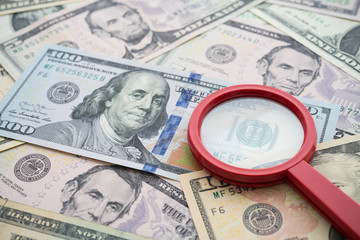 Red magnifying glass on US dollars paper banknote bill background. Concept of find out refinance,...