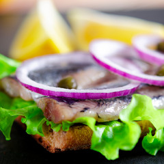 Appetizing smorrebrod with Norwegian herring, lettuce, blue onion, lemon and tomato lies on a...