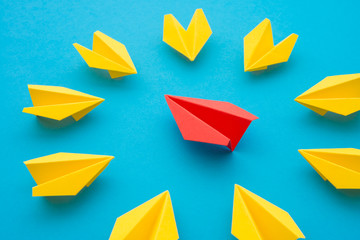 Leadership concept. Red paper plane origami leading among small yellow planes on blue background....