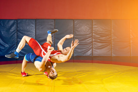 Two greco-roman  wrestlers in red and blue uniform wrestling  on a yellow wrestling carpet in the gym