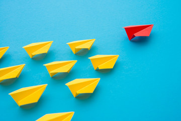 Leadership concept. Red paper plane origami leading among small yellow planes on blue background....