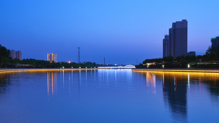 Fototapeta premium Night view of city buildings and river with blue background
