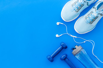 Fitness background with sneakers, dumbbells and headphones on blue table top view copy space
