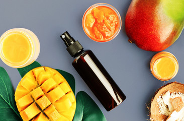 Summer spa skincare with fresh tropical fruit ingredient, top view blue backgound. Mango facial mask and spray bottle of sunscreen lotion. Nourishing body care.