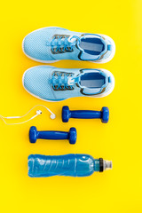 Fototapeta na wymiar Athletics flat-lay with dumbbells, water. sneakers on yellow background top-down